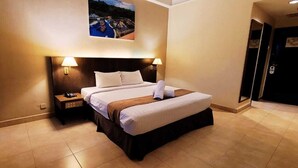 A hotel room with a bed, bedside tables, a nightstand, a wall-mounted lamp, and a painting above the bed. - Amverton Heritage Resort (Malacca City)