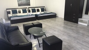 Un salon moderne avec un canapé, des poufs, une table basse en verre et un lit avec une literie bleue et blanche.