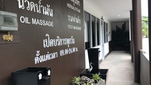 Un couloir avec un mur où sont affichées les prestations proposées, comme les soins du visage, les massages à l’huile et les soins des pieds, ainsi qu’un comptoir d’accueil agrémenté de plantes.