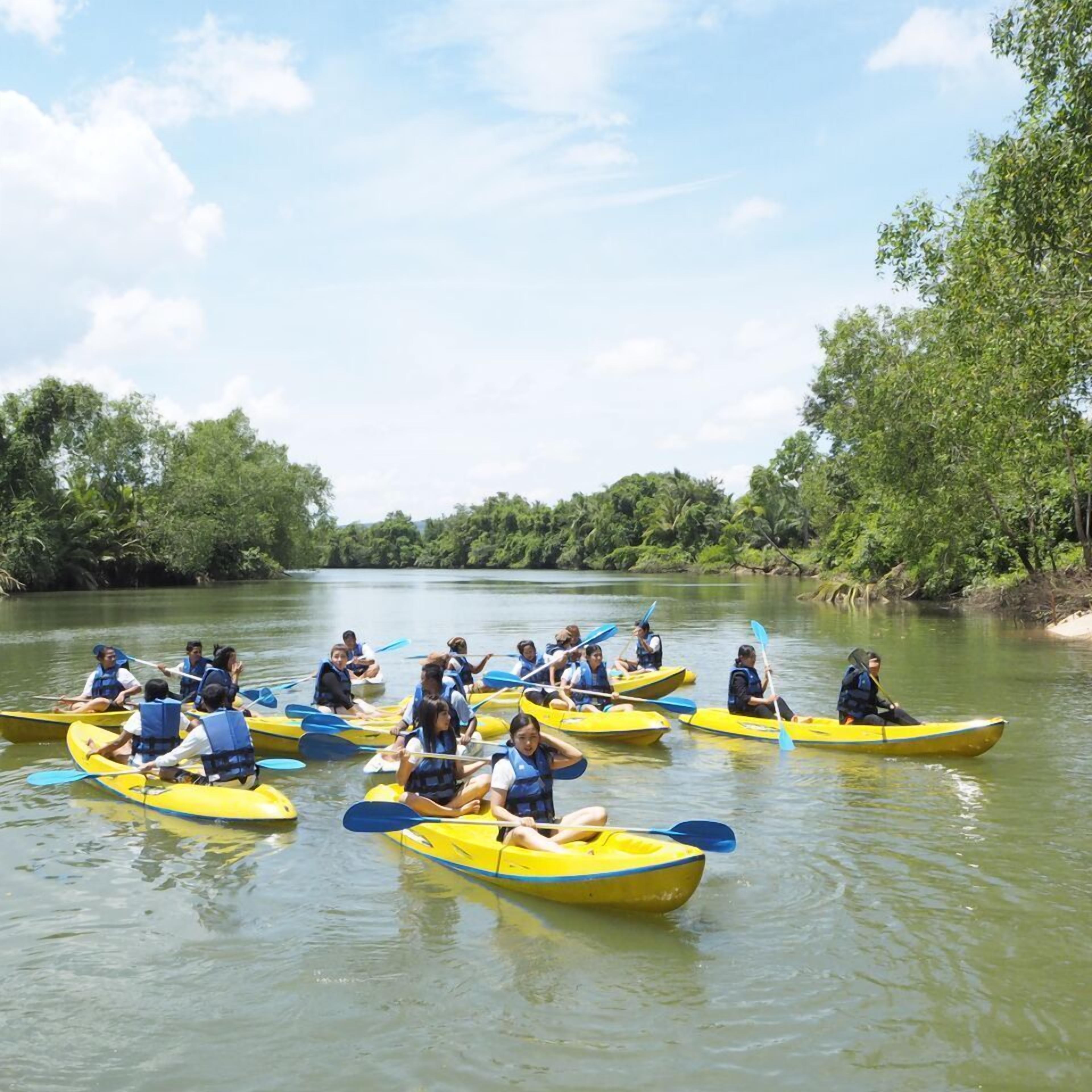 Eine Gruppe von Menschen in gelben Kanus auf einem ruhigen Fluss, umgeben von viel Grün.