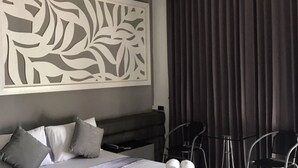 Une chambre d’hôtel moderne avec un grand lit, une literie grise, un élément décoratif mural et une vue sur l’extérieur à travers des rideaux foncés.