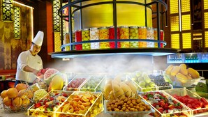 A buffet with various fruits and vegetables, a chef preparing food, and a decorative ceiling.