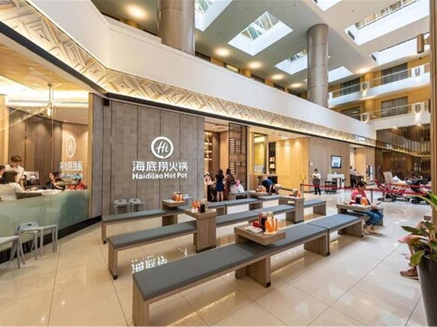 A modern hotel lobby with a seating area, a restaurant, and a visible sign for Haidilao Hot Pot.