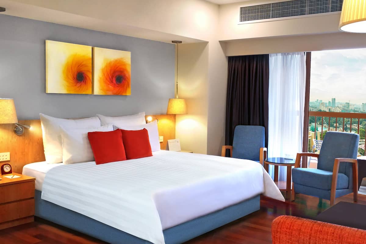 Quarto de hotel com uma cama grande, duas mesas de cabeceira, uma cadeira e vista para a cidade.