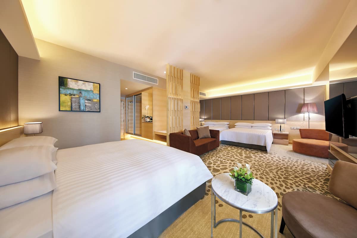 Quarto de hotel com uma cama grande, dois sofás, uma mesinha com uma planta e uma televisão.
