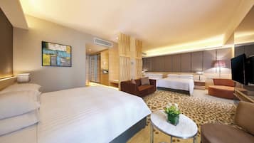 A hotel room with a large bed, two sofas, a small table with a plant, and a TV.