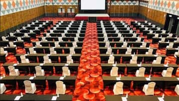 A conference room with rows of tables and chairs, a stage at the front, and a patterned wall.