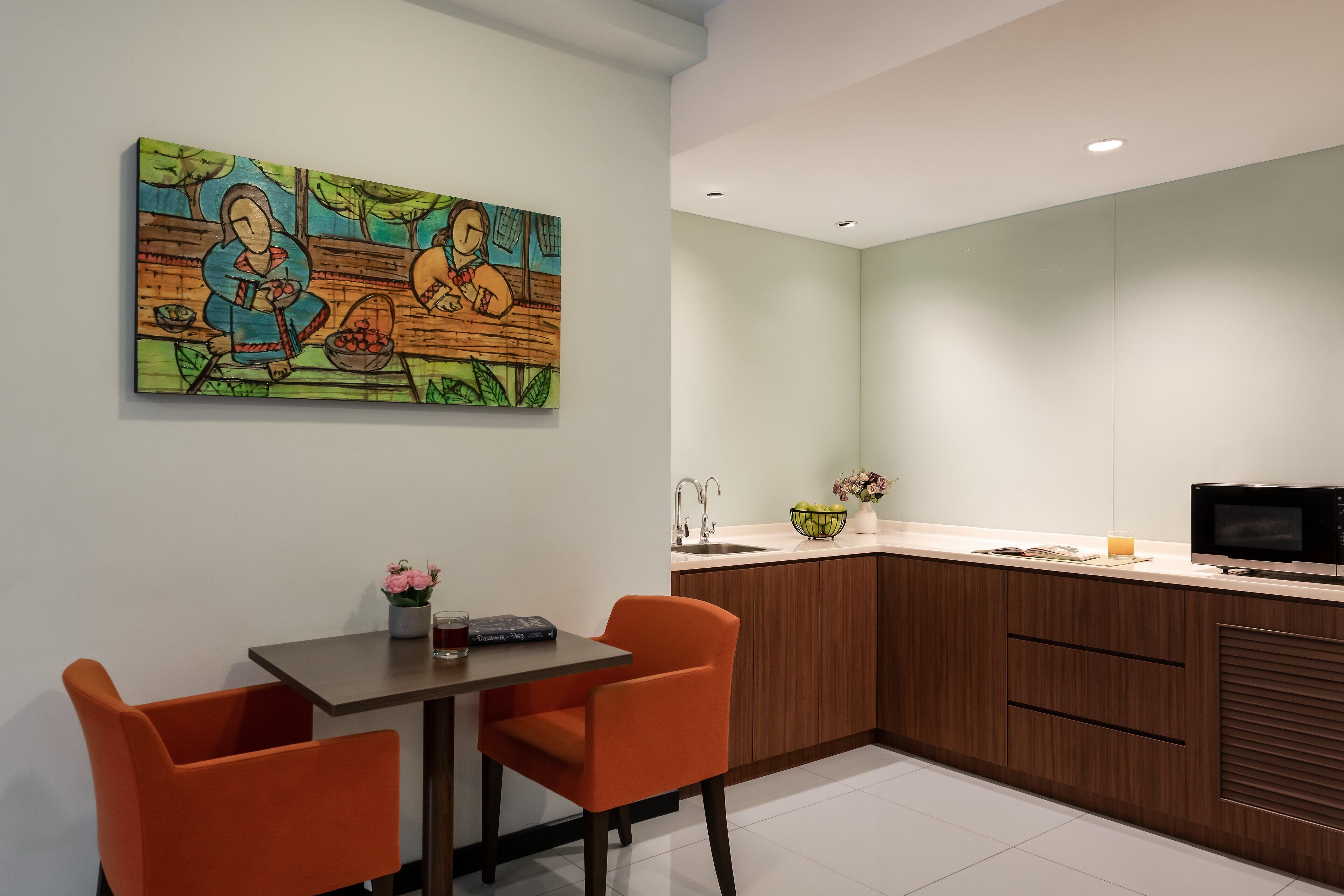 Una cocina moderna con armarios de madera, una mesa de comedor con dos sillas y un cuadro de colores en la pared.