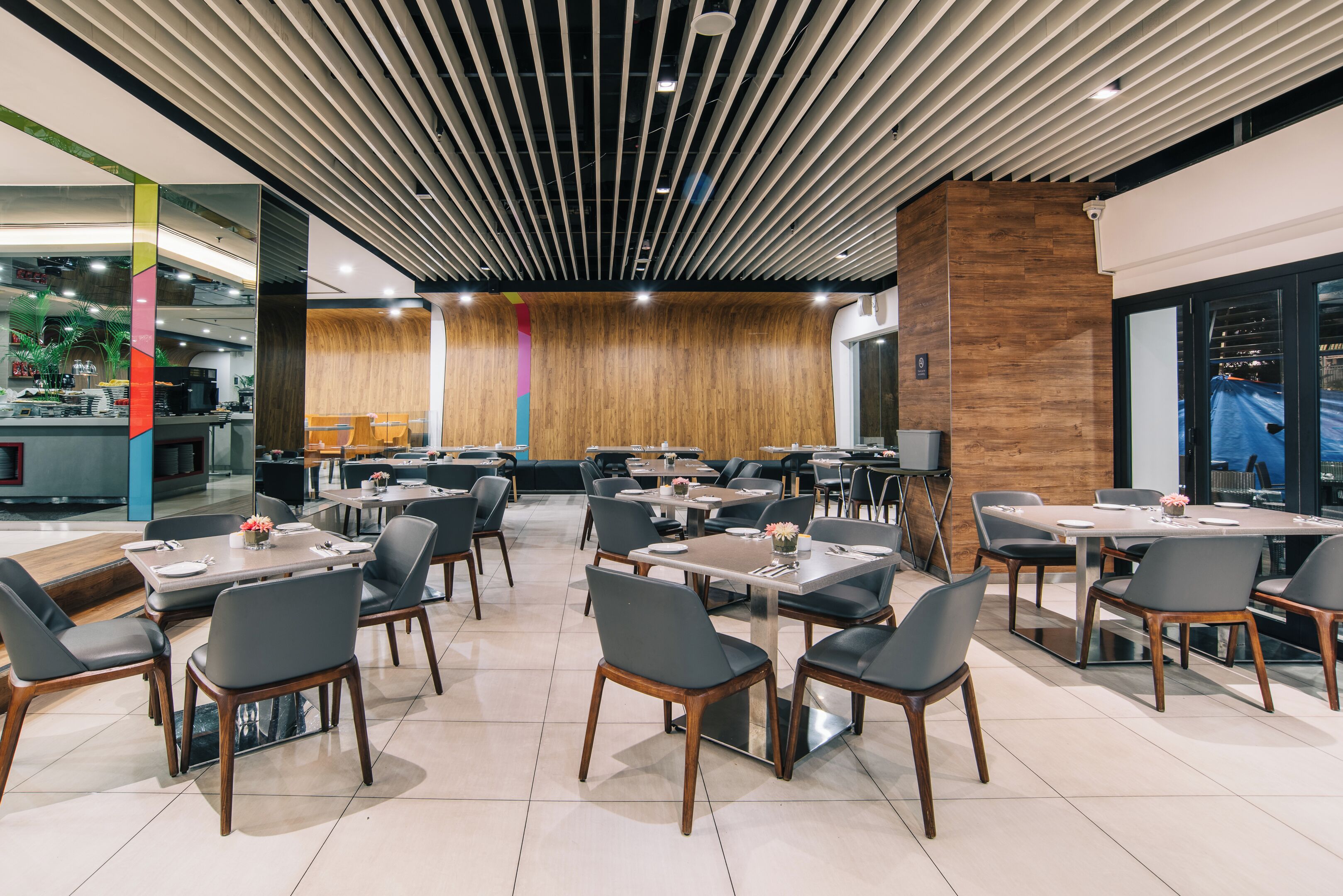 A modern restaurant with a wooden accent wall, multiple dining tables, and black chairs.