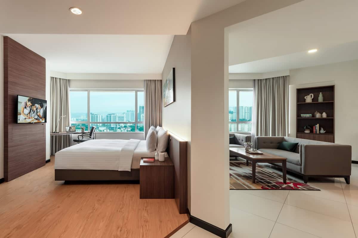 A modern hotel room with a large bed, a desk, a sofa, and a view of the cityscape.