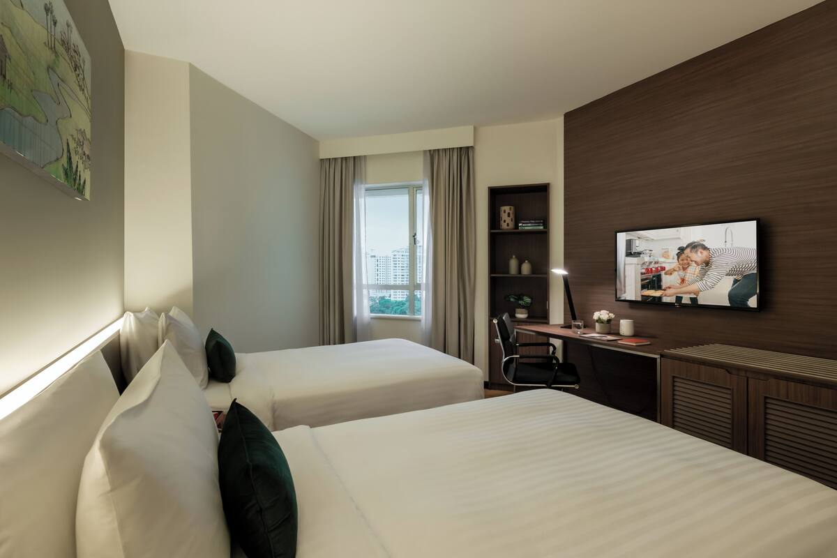 A hotel room with two beds, a desk, a chair, a television, and a window with curtains.