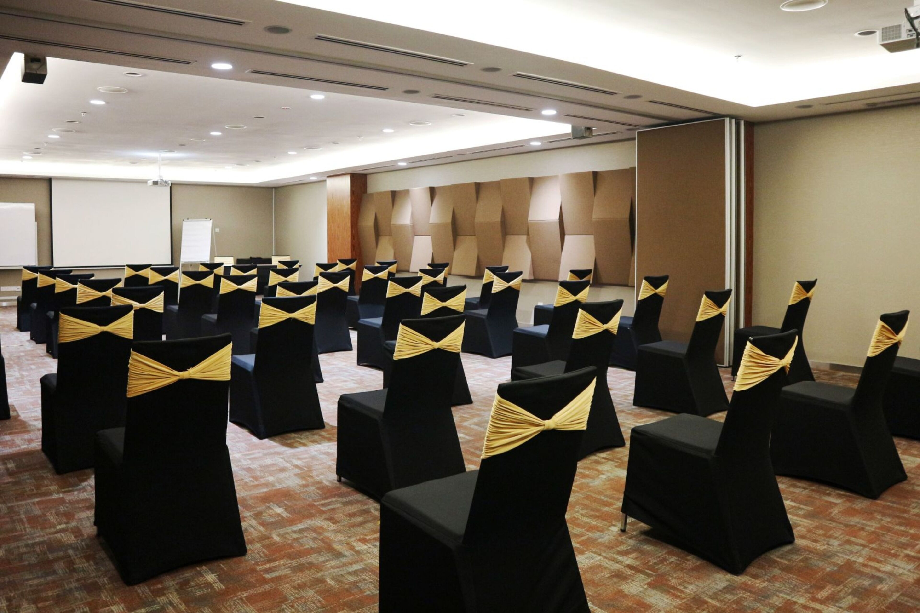 A conference room with rows of black chairs with gold sashes, a whiteboard, and a projector screen.