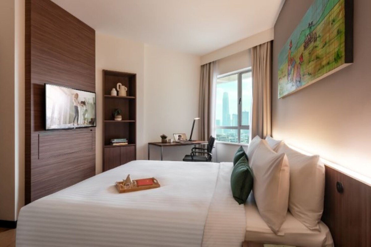 A hotel room with a bed, a desk, a TV, a bookshelf, and a painting on the wall.