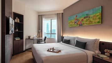 A hotel room with a large bed, a desk, a chair, a bookshelf, and a painting on the wall.