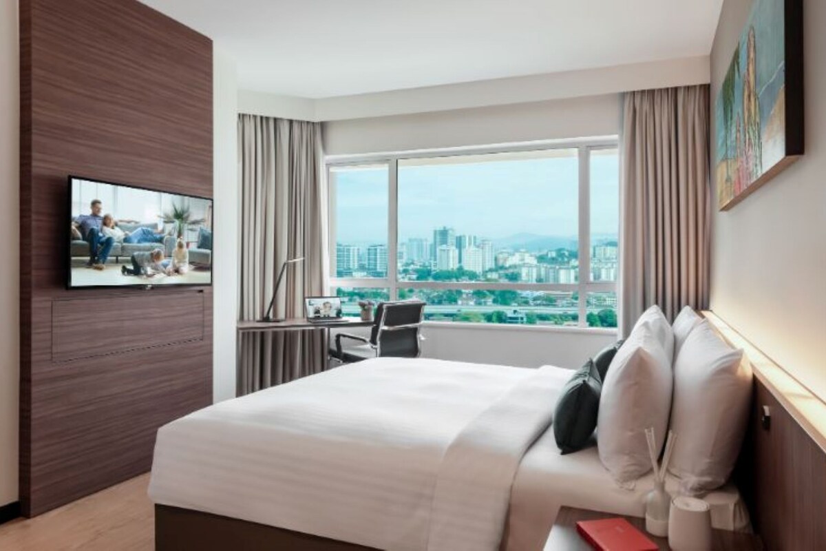 A hotel room with a bed, a desk, a chair, a TV, and a large window with a city view.