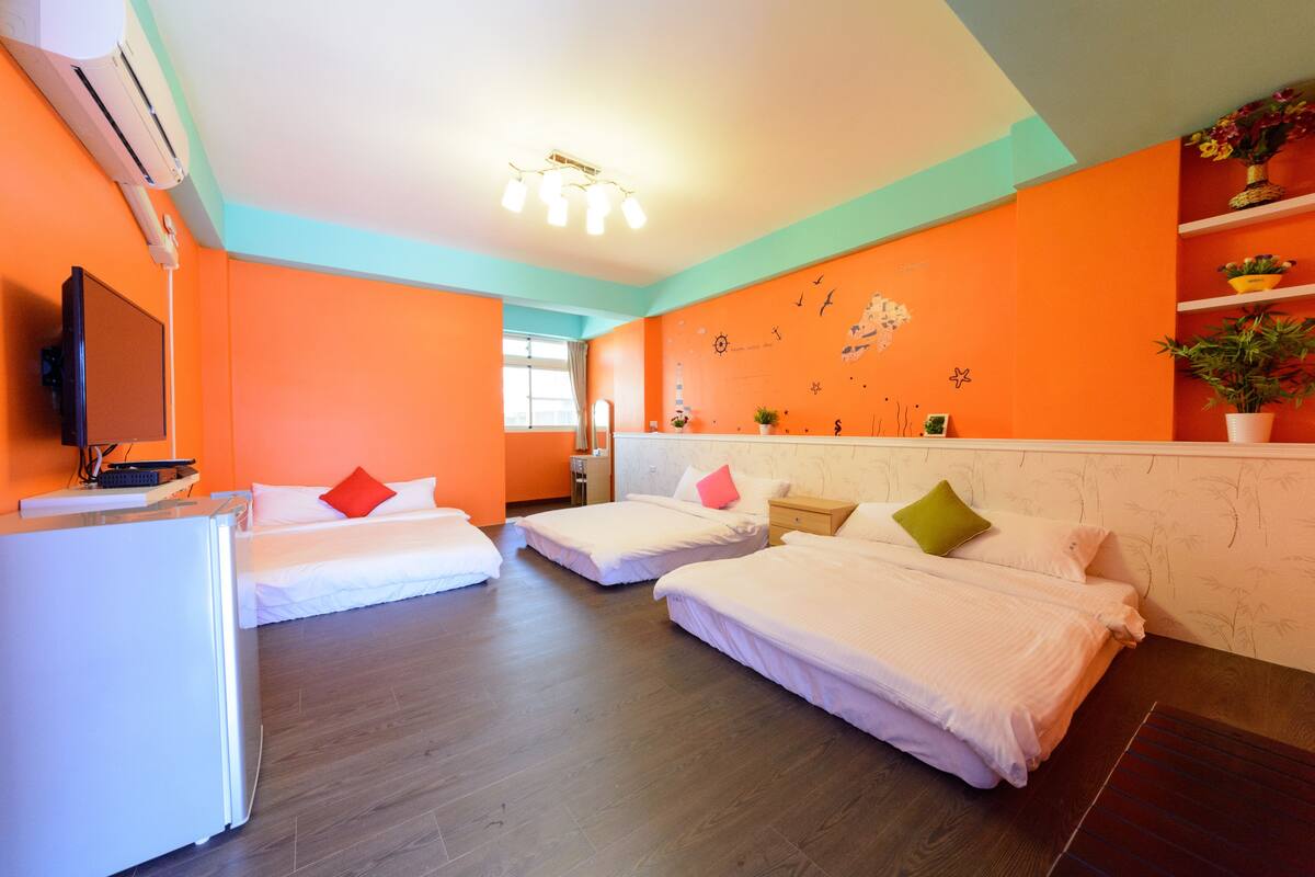 Quarto de hotel com três camas, televisão, frigorífico e parede decorada com autocolantes de tema náutico.