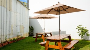A wooden picnic table with two umbrellas and benches, surrounded by a well-maintained lawn and potted plants. - Shell Hotel (Hengchun)
