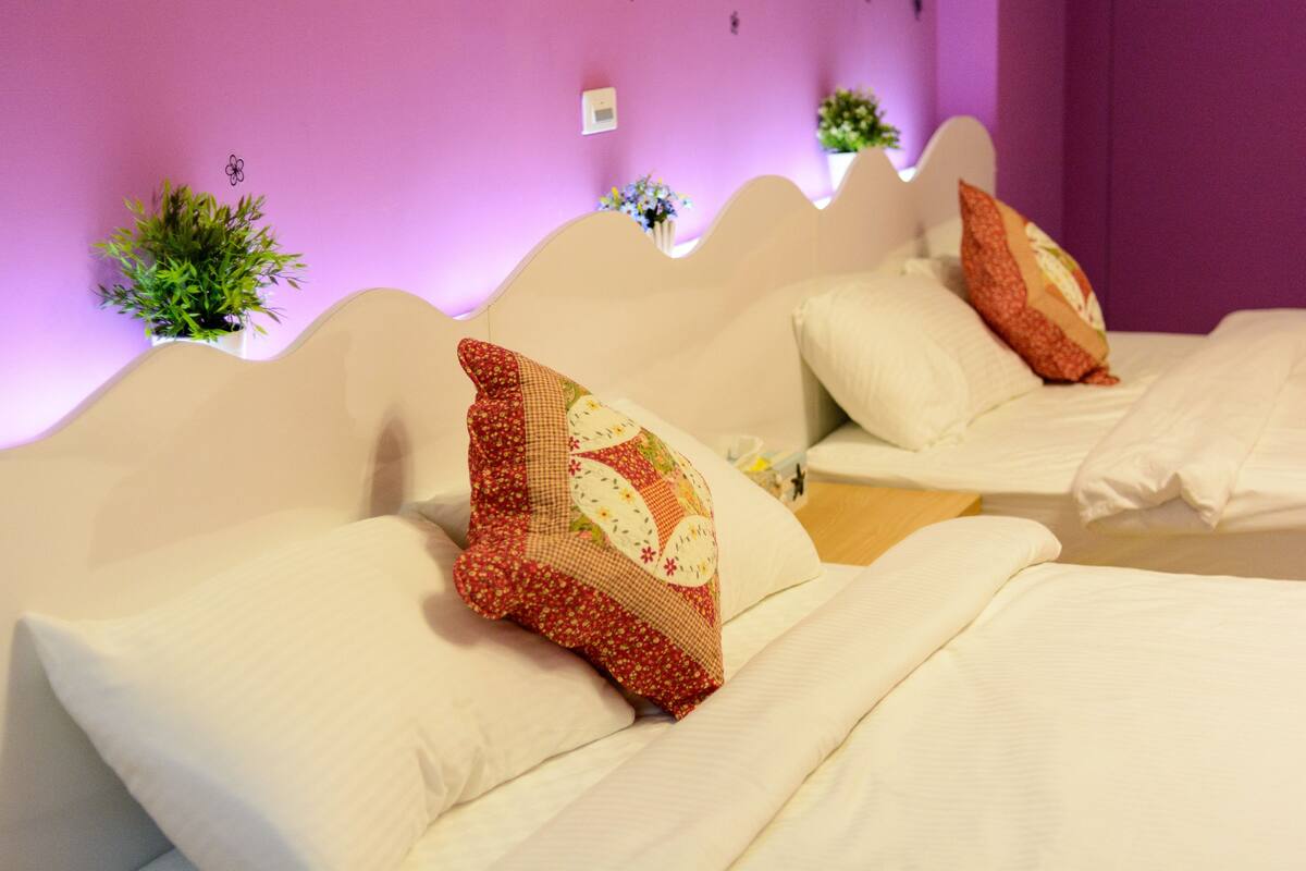 Quarto de hotel com um design de cabeceira ondulada, várias almofadas e pequenas plantas em vasos na parede.