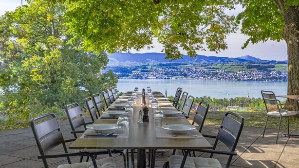 A table set for dining with chairs, overlooking a lake and a town.