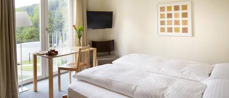 A hotel room with a bed, a desk with a chair, a TV, and a window with curtains.