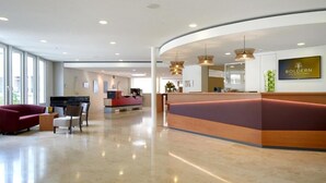 A modern hotel lobby with a reception desk, seating area, and large windows.