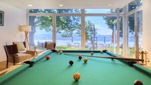 A pool table with balls, a sofa, and a view of a lake through large windows.