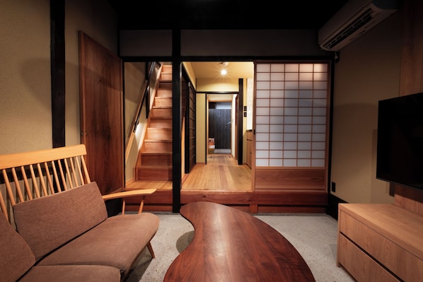 A traditional Japanese interior with a wooden staircase, tatami flooring, a low wooden table, and a television.
