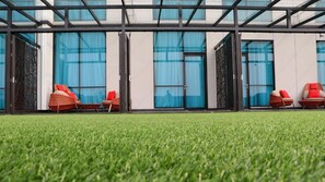 A modern building with large glass windows and doors, outdoor seating with wicker chairs and red cushions, and a well-maintained lawn. - Luminor Hotel Pecenongan Jakarta by WH (Jakarta)