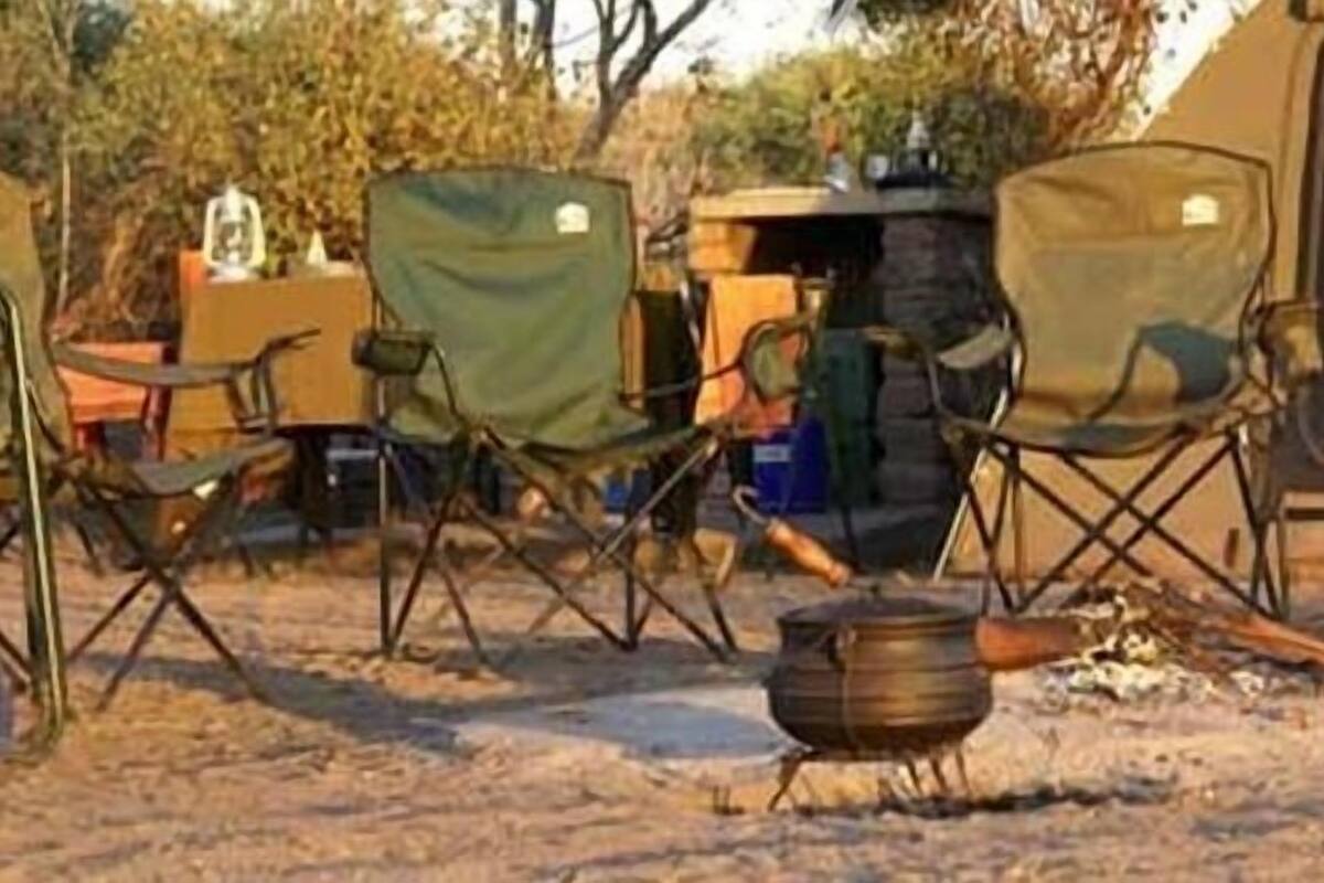 A campsite with four camping chairs, a portable stove, and a tent in the background.