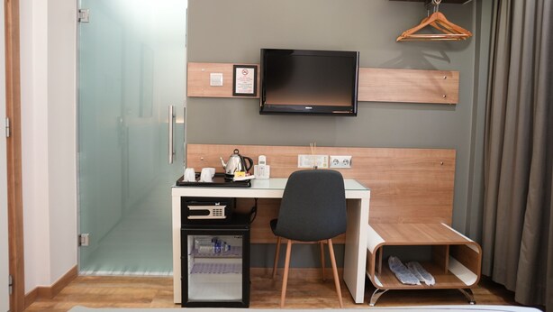 A hotel room with a desk, chair, television, minibar, and a shoe rack. - My Dora Hotel (Istanbul)
