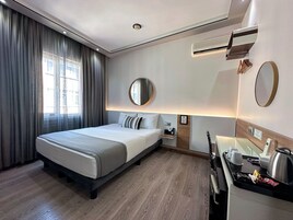A hotel room with a bed, bedside table, mirror, and a kitchenette area.