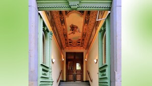 Eine Treppe mit grün gestrichenen Geländern und Fliesenboden führt zu einer Tür mit einer verzierten Decke.