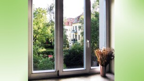 Ein großes Fenster mit mehreren Scheiben, das einen Blick auf ein Wohngebiet mit Bäumen und Häusern freigibt.