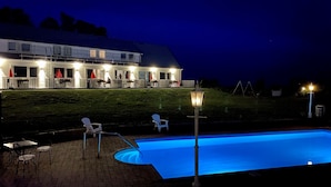 A swimming pool with a blue-lit edge, outdoor seating, and a building with illuminated windows in the background. - Löderups Strandbad Hotell & Stugby (Loderup)