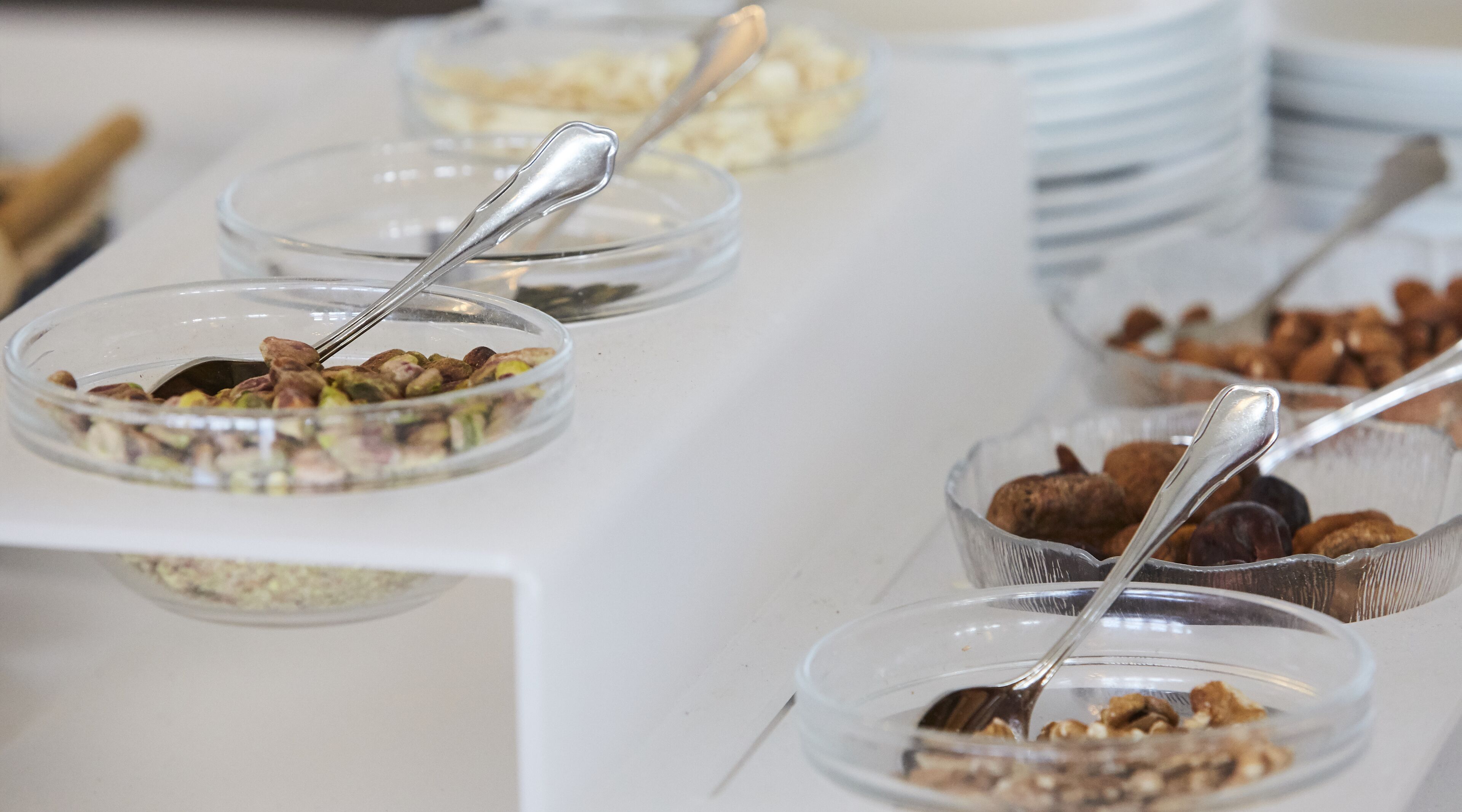 Una mesa de buffet con diversos alimentos en recipientes de vidrio transparente, cada uno con una cuchara.