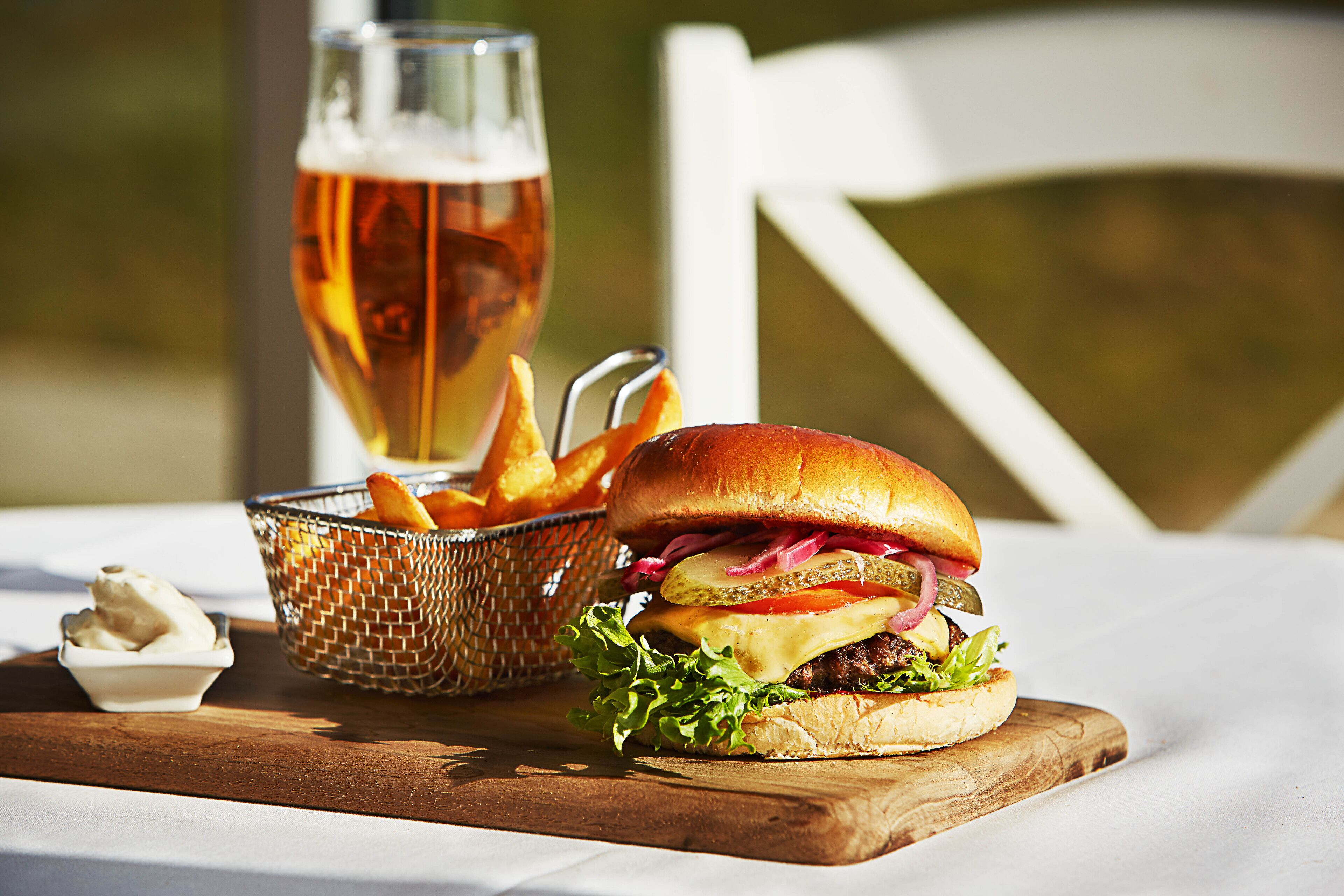 A meal with a burger, fries, and a glass of beer on a wooden board.