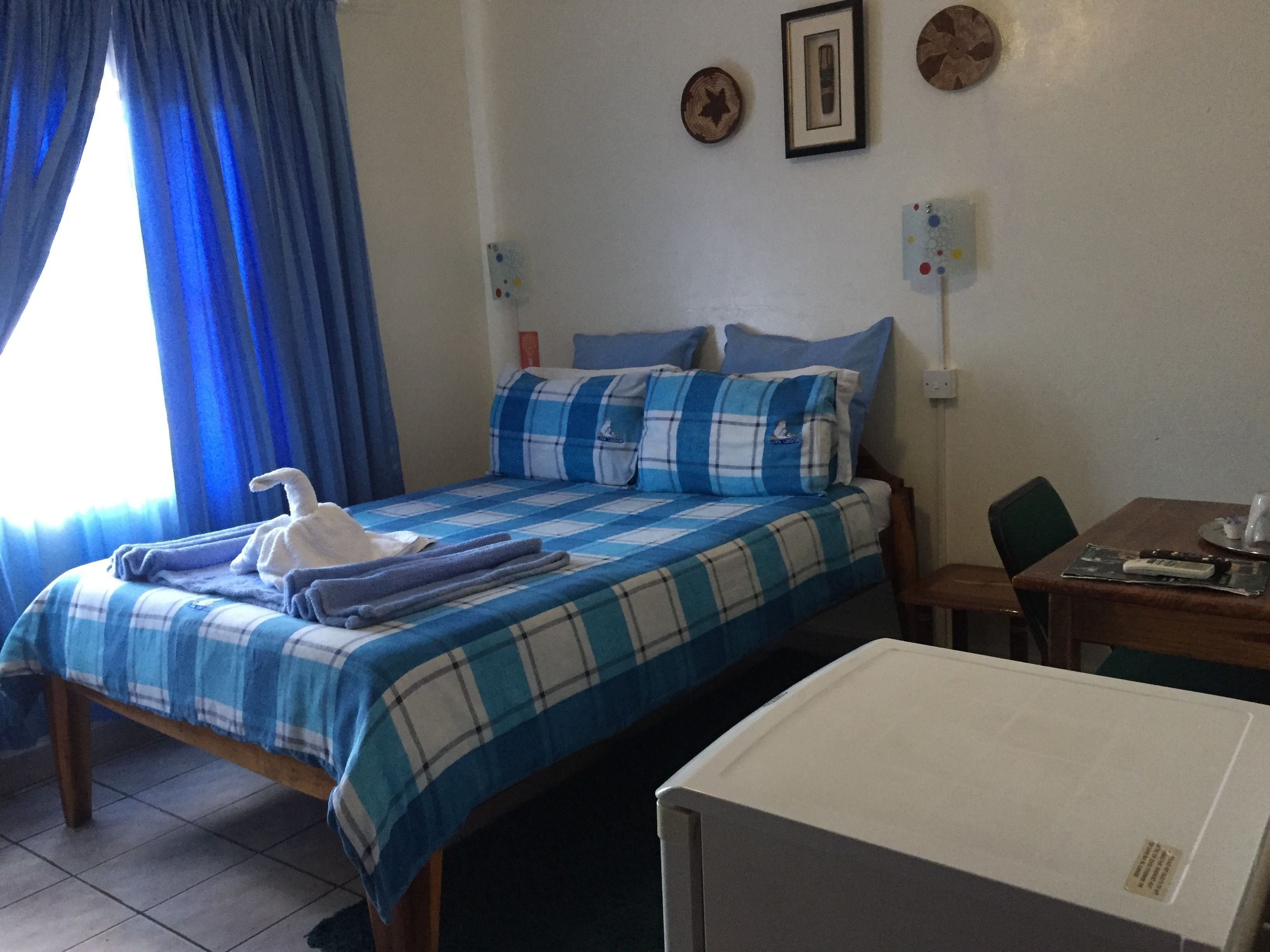 Habitación de hotel con cama, escritorio y silla. Hay cortinas en la ventana y un reloj de pared.