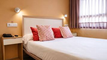 A hotel room with a bed, two bedside tables, a telephone, and a wall socket.