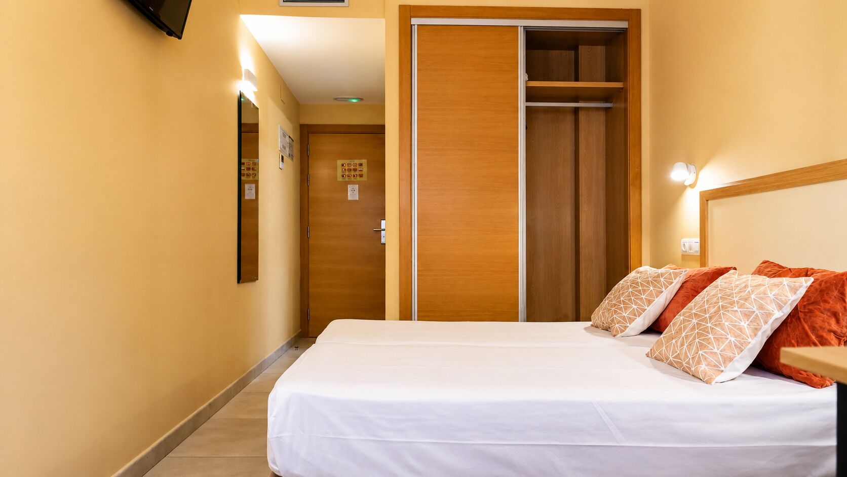 A hotel room with a bed, a wardrobe, and a mirror.