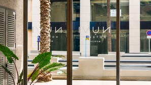 Entrada de un hotel con una palmera, una puerta de cristal y un cartel con el nombre del hotel.