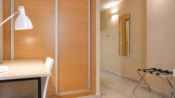A hotel room with a wooden partition, a desk with a white lamp, a chair, and a trolley.