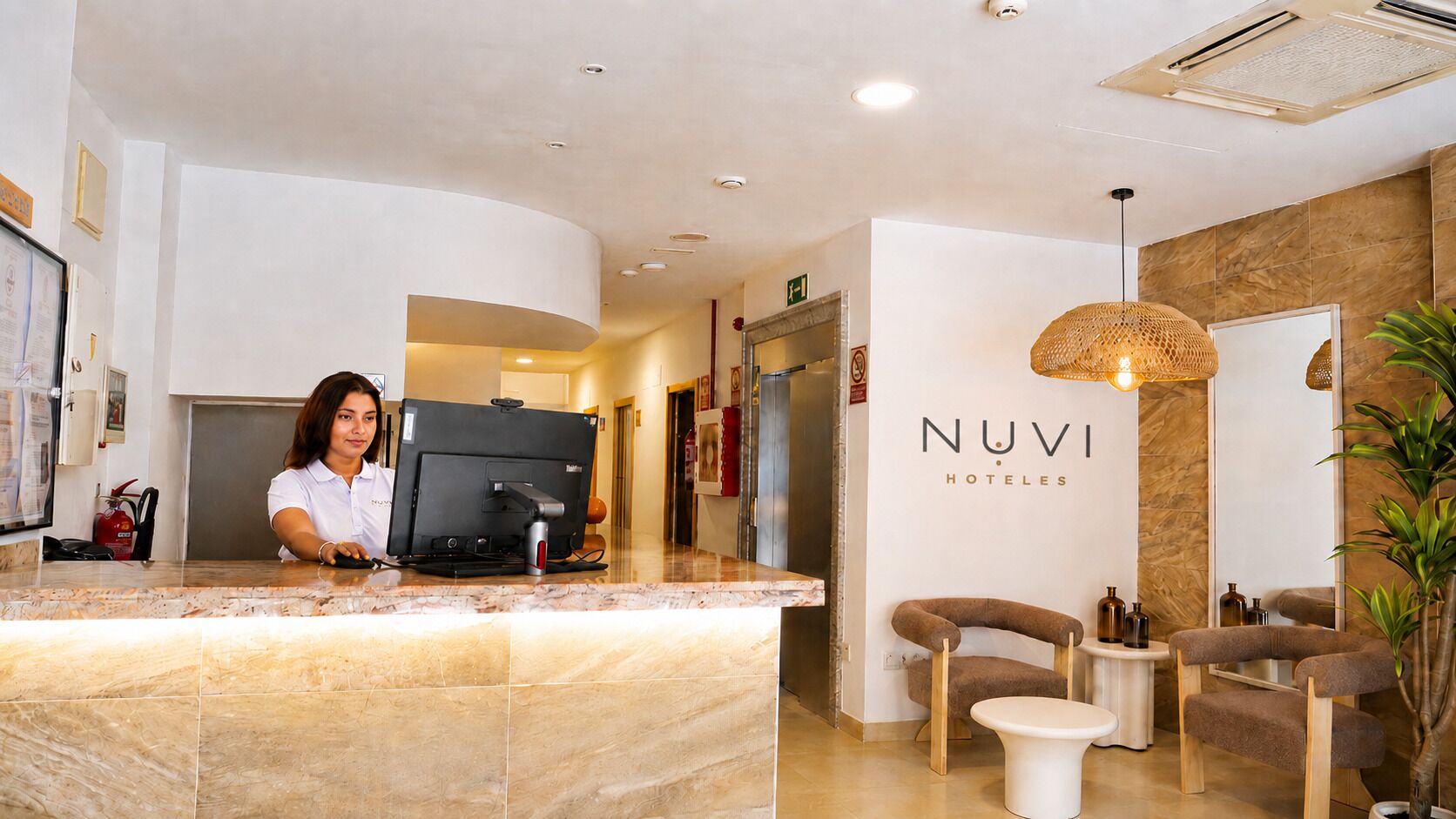 Zona de recepción con una recepcionista, una computadora y un letrero de Nuvi Hotels.