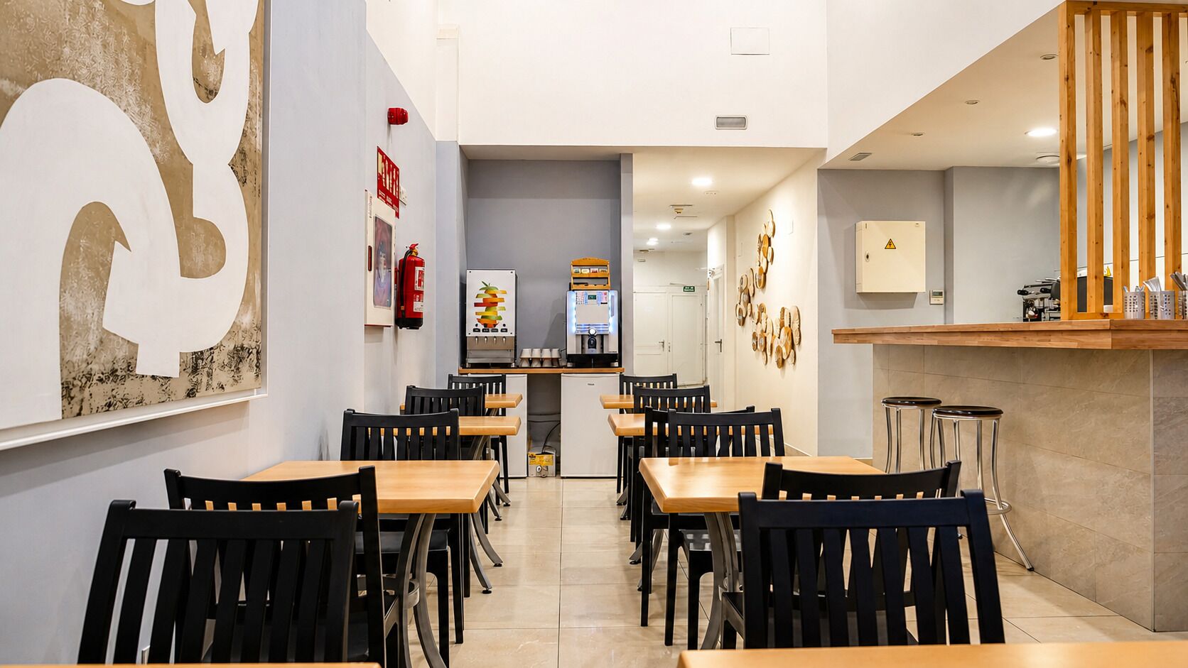 Un interior de restaurante con varias mesas y sillas, una zona de cocina y una barra.