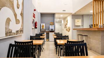 Un interior de restaurante con varias mesas y sillas, una zona de cocina y una barra.