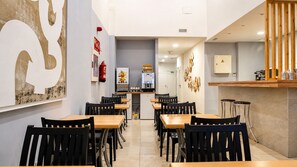 Un interior de restaurante con varias mesas y sillas, una zona de cocina y una barra.