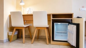 A compact kitchenette with a refrigerator, two chairs, a small table, and a lamp.