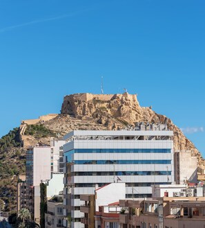 Un edificio moderno con tejado plano y múltiples ventanas, ubicado en una colina con un afloramiento rocoso al fondo.