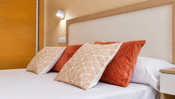 A bed with three pillows, a bedside table, and a wall-mounted light.