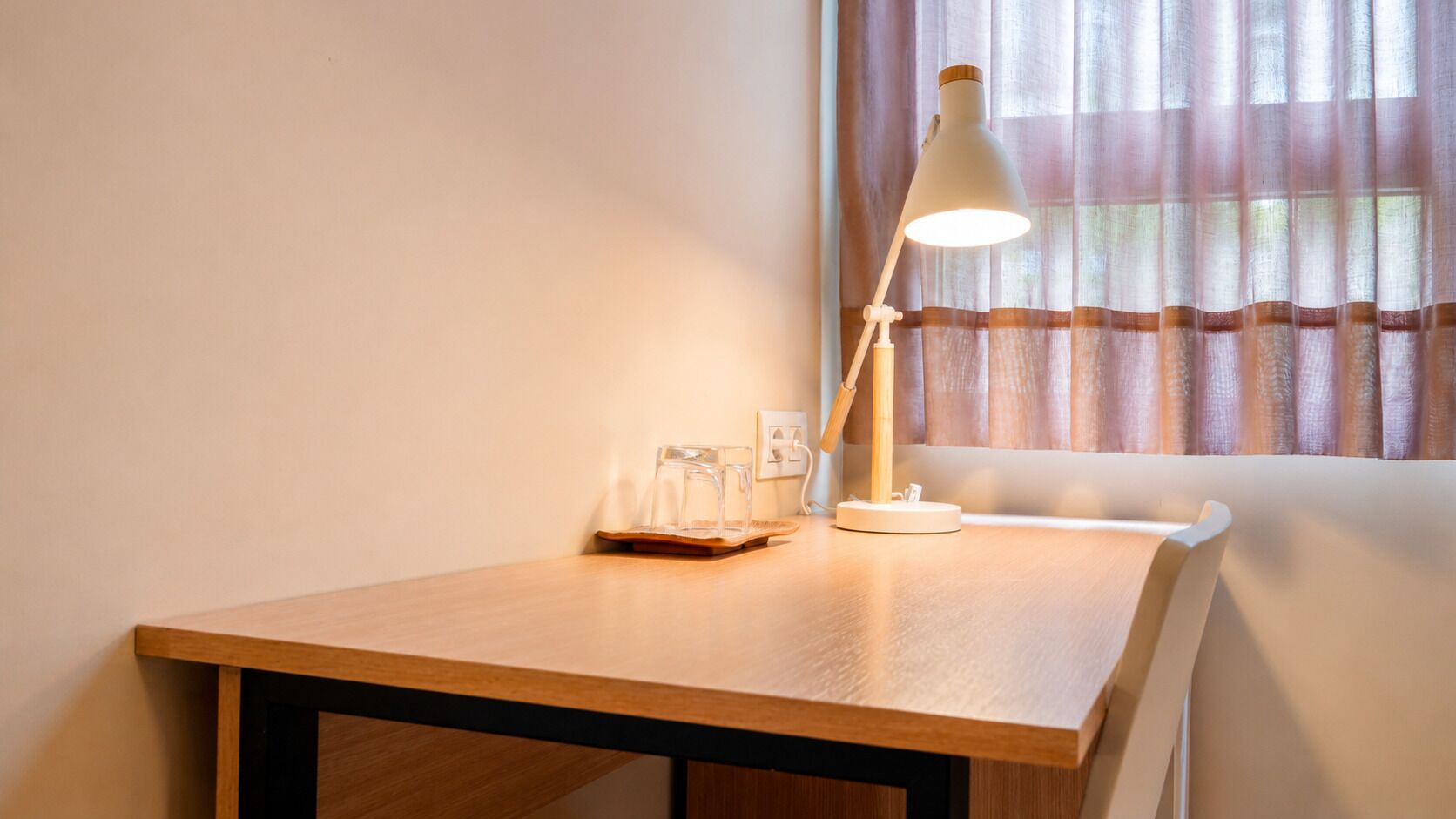 Una mesa de madera con una lámpara de escritorio blanca, un vaso y una caja de pañuelos.