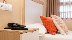 Habitación de hotel con cama, mesita de noche con teléfono y controles remotos, y ventana con cortinas.
